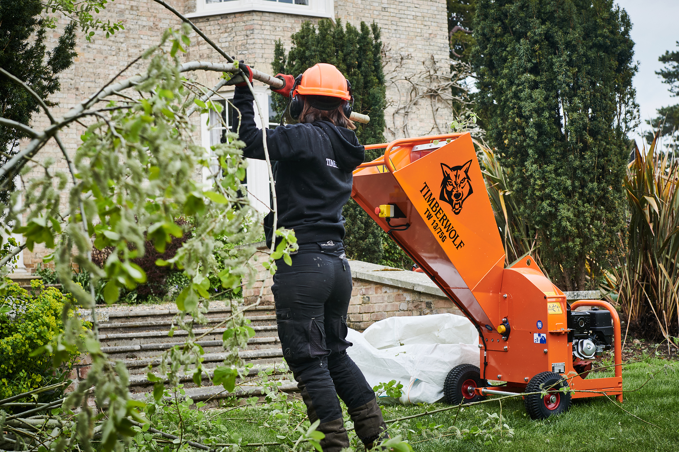 chipper2 Person feeding tree branches into an orange Timberwolf wood chipper machine in a garden