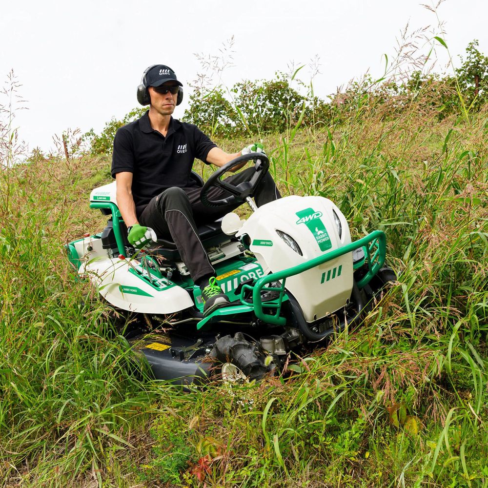 Operator riding white and green Orec Rabbit brushcutter cutting tall grass on slope