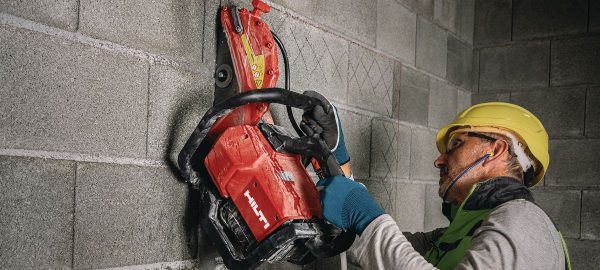 Worker wearing safety gear using a red Hilti disc cutter to cut a vertical concrete wall
