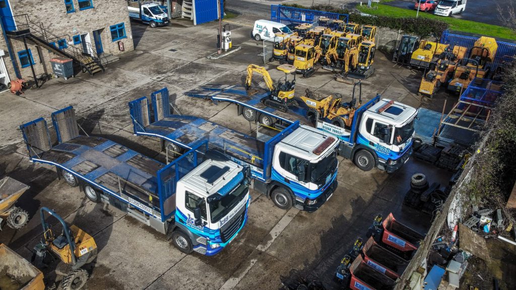 Aerial view of blue flatbed trucks and construction equipment in a yard